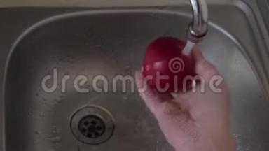 一个人在流水下揉搓洗一个成熟的<strong>红<strong>苹果</strong>。 素食者准备零食。 右手和<strong>水果</strong>